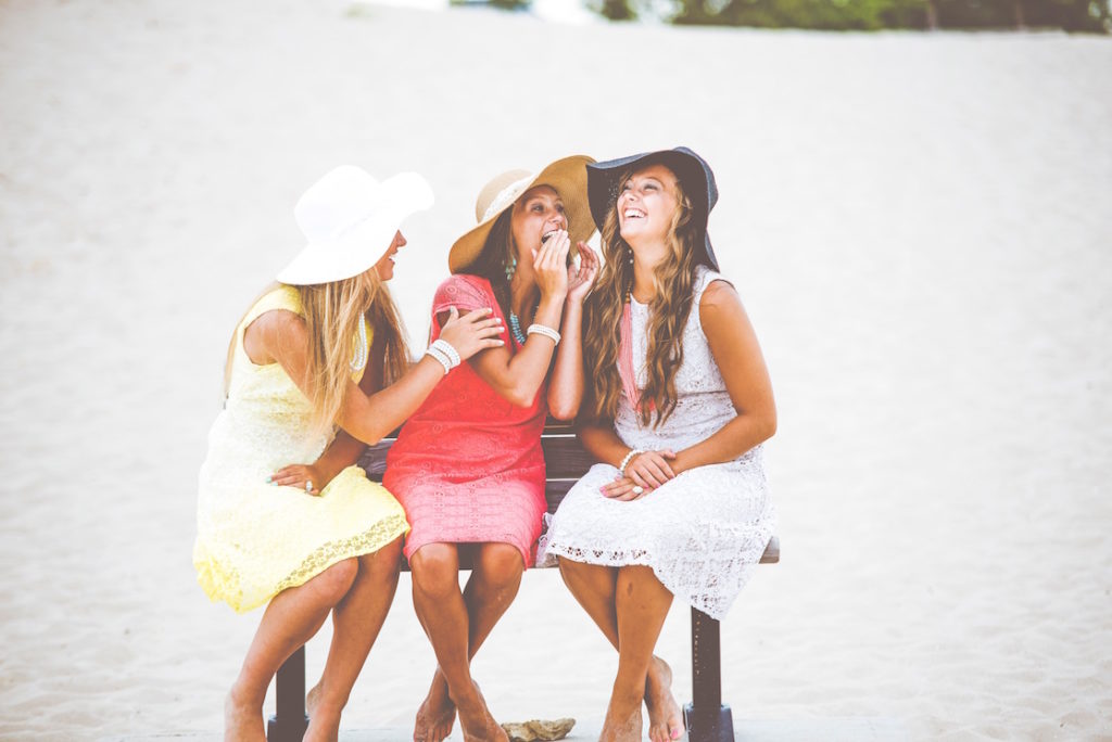 Kolme nuorta naista istuvat rannalla ja nauravat