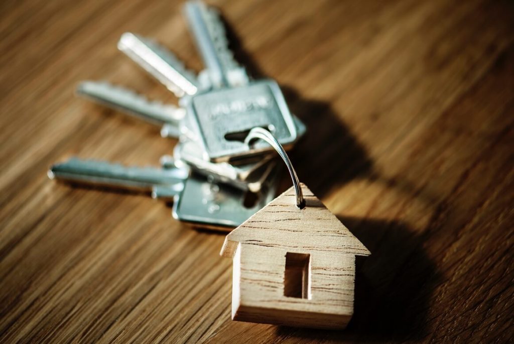 Juuri ostetun asunnon avaimet pöydällä puisen talonmuotoisen avaimenperän kanssa