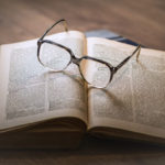 Kuva aukiolevasta sanakirjasta, jonka päällä on silmälasit