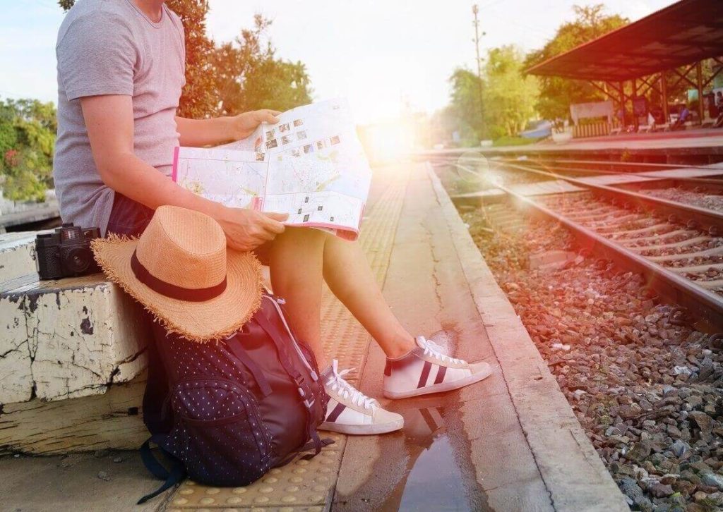 Matkailija istuu juna-asemalla lukemassa karttaa