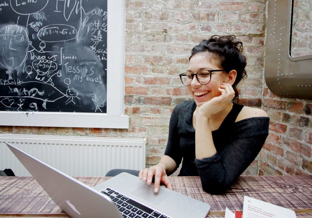 Nuori hymyilevä nainen täyttää opintolainan hakemusta kannettavalla tietokoneella