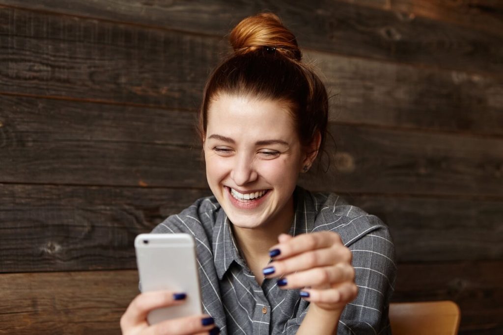 Hymyilevä tyttö kokeilee Raha.fi:n maksutonta palvelua kännykkänsä kautta