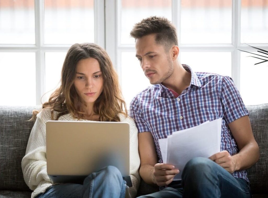 Huolestuneen näköinen pariskunta istuu sohvallaan ja katsovat kannettavalta tietokoneelta saamaansa hylättyä lainapäätöstä