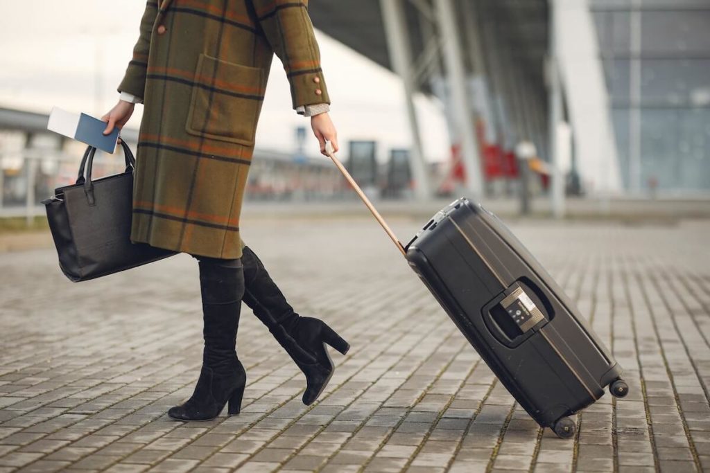 Nainen, jolla on matkavakuutus, vetää matkalaukkua lentokentällä